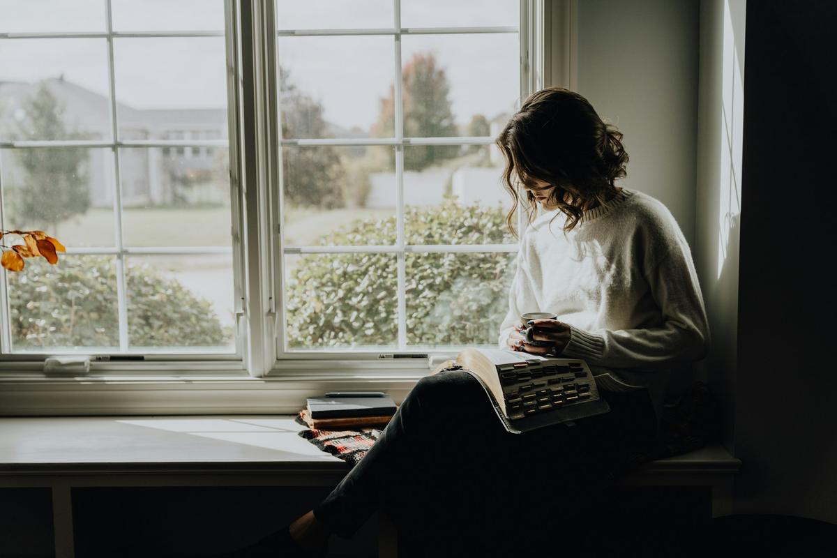 A woman reading by the window with a mug